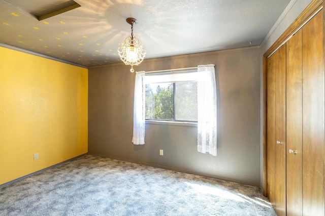 unfurnished bedroom with carpet, a closet, crown molding, a textured ceiling, and a chandelier