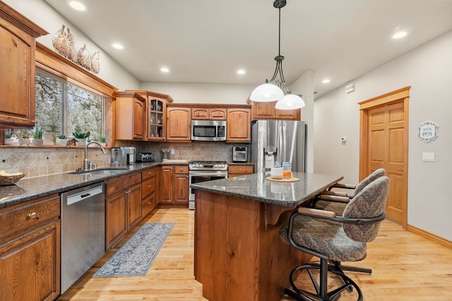 kitchen with a kitchen island, stainless steel appliances, sink, light hardwood / wood-style flooring, and a breakfast bar area