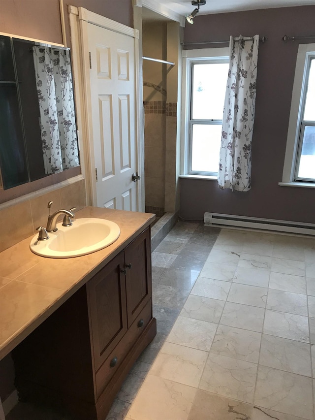 bathroom featuring vanity, a tile shower, baseboard heating, and tasteful backsplash