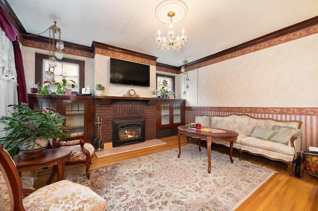 living room with a chandelier, hardwood / wood-style floors, a brick fireplace, and ornamental molding