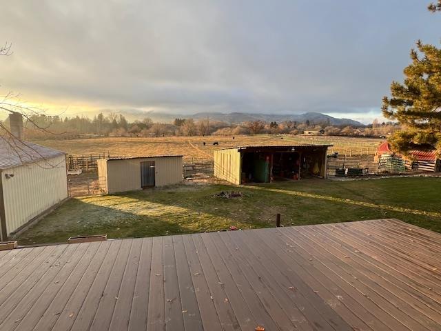 deck at dusk featuring an outbuilding, a rural view, and a lawn