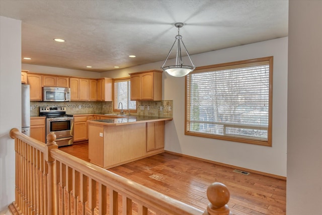 kitchen featuring pendant lighting, light brown cabinetry, appliances with stainless steel finishes, light hardwood / wood-style floors, and kitchen peninsula