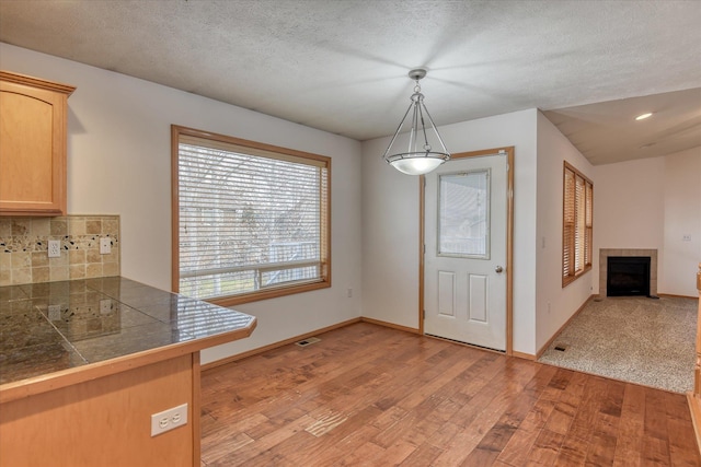 unfurnished dining area with a tile fireplace, a textured ceiling, and light hardwood / wood-style floors