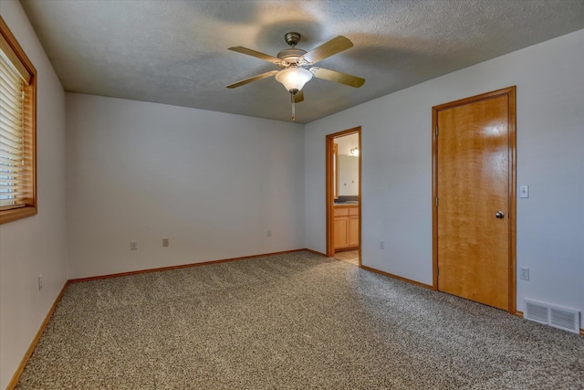 unfurnished bedroom with ceiling fan, ensuite bathroom, light colored carpet, and a textured ceiling