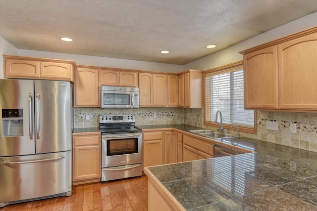 kitchen with light brown cabinetry, sink, stainless steel appliances, and light hardwood / wood-style flooring