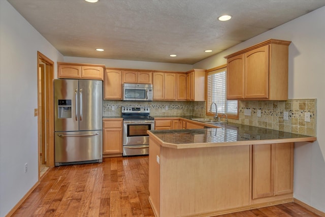 kitchen with kitchen peninsula, appliances with stainless steel finishes, light wood-type flooring, and sink