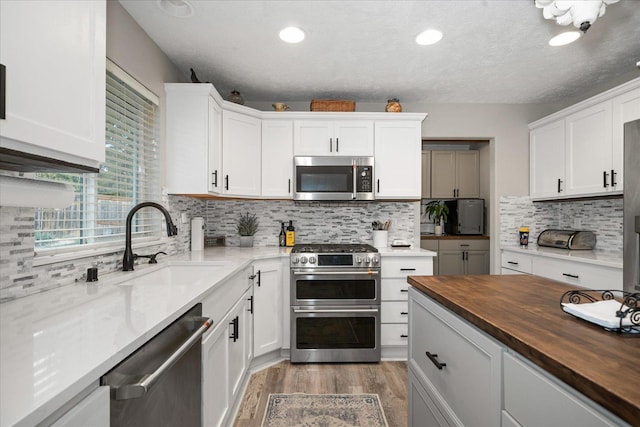 kitchen featuring stainless steel appliances, butcher block countertops, white cabinetry, and sink