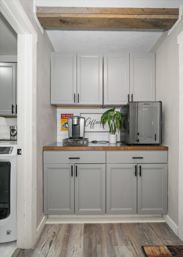 bar featuring tasteful backsplash, washer / clothes dryer, light hardwood / wood-style floors, and beam ceiling