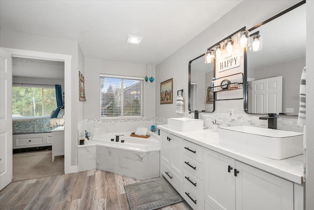 bathroom featuring hardwood / wood-style floors, a relaxing tiled tub, vanity, and a wealth of natural light