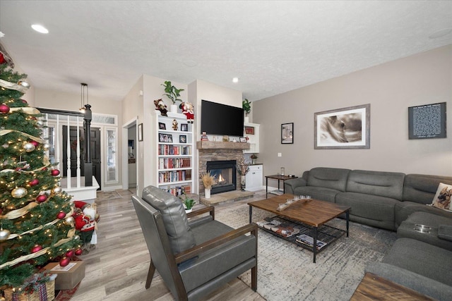 living room featuring a textured ceiling, light hardwood / wood-style floors, and a stone fireplace