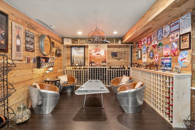 wine area featuring hardwood / wood-style floors, wooden walls, and an inviting chandelier