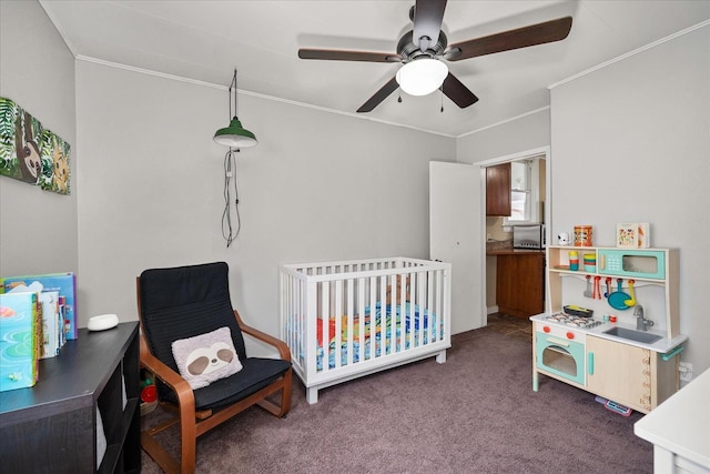 bedroom featuring dark colored carpet, ceiling fan, a crib, and crown molding