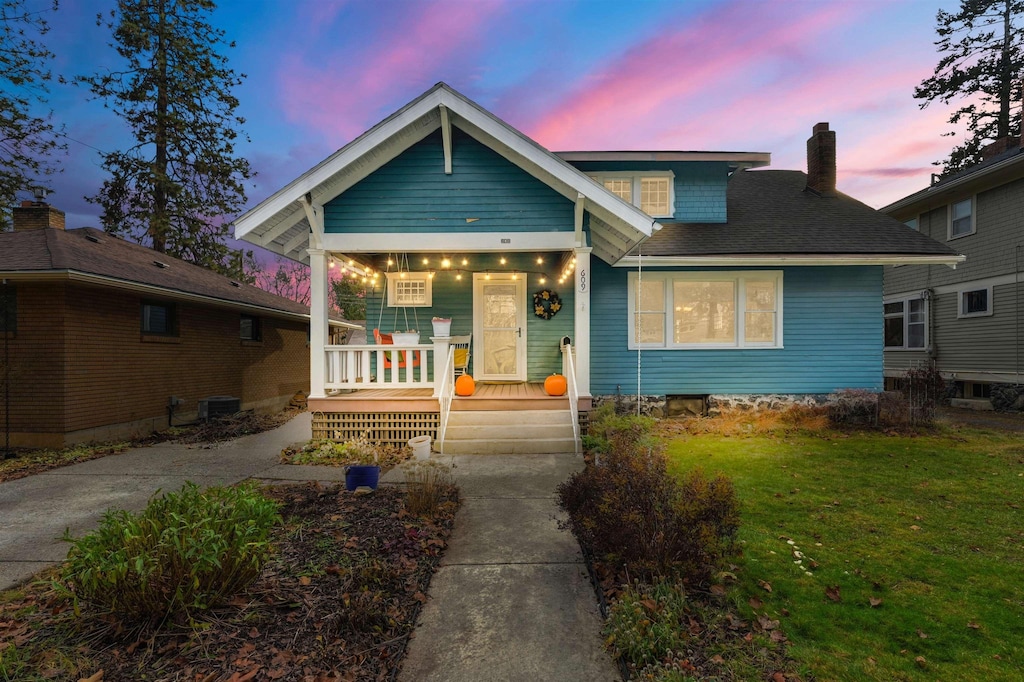 view of front of home featuring a porch, cooling unit, and a lawn