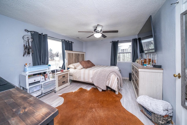 bedroom with ceiling fan, light hardwood / wood-style floors, a textured ceiling, and multiple windows