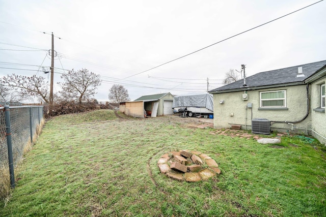 view of yard with a garage, an outdoor structure, central AC unit, and an outdoor fire pit