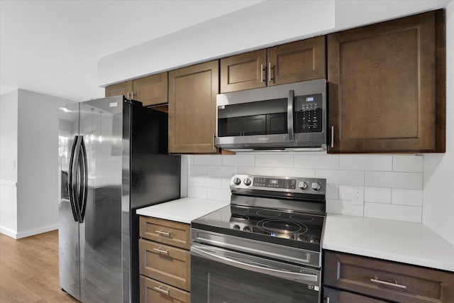 kitchen with light wood-type flooring, stainless steel appliances, dark brown cabinetry, and backsplash