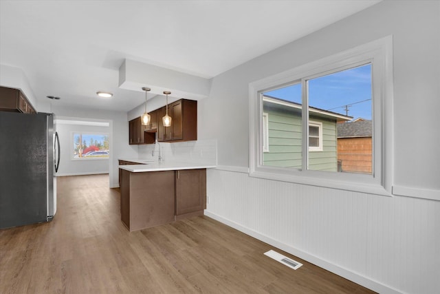 kitchen with kitchen peninsula, light wood-type flooring, sink, pendant lighting, and stainless steel refrigerator