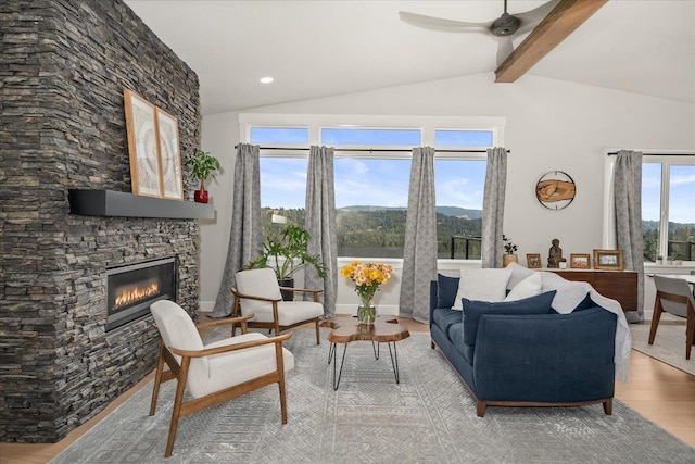 living room with a stone fireplace, ceiling fan, lofted ceiling with beams, and hardwood / wood-style flooring