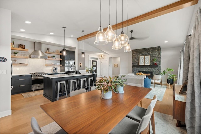 dining room with a fireplace, vaulted ceiling with beams, and light hardwood / wood-style floors