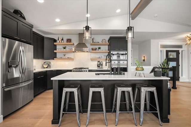 kitchen featuring appliances with stainless steel finishes, light wood-type flooring, wall chimney exhaust hood, and an island with sink