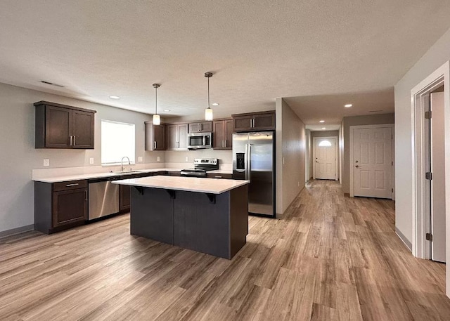 kitchen with sink, hanging light fixtures, appliances with stainless steel finishes, a kitchen island, and light wood-type flooring