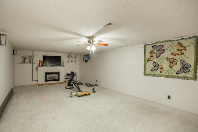 exercise area featuring ceiling fan, carpet floors, a textured ceiling, and a brick fireplace