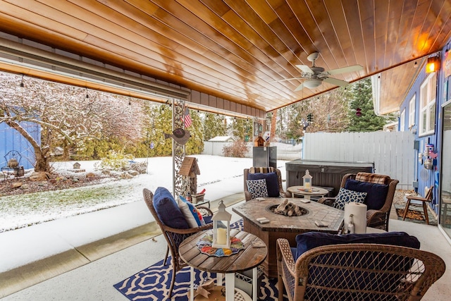 snow covered patio with ceiling fan, an outdoor fire pit, and a hot tub