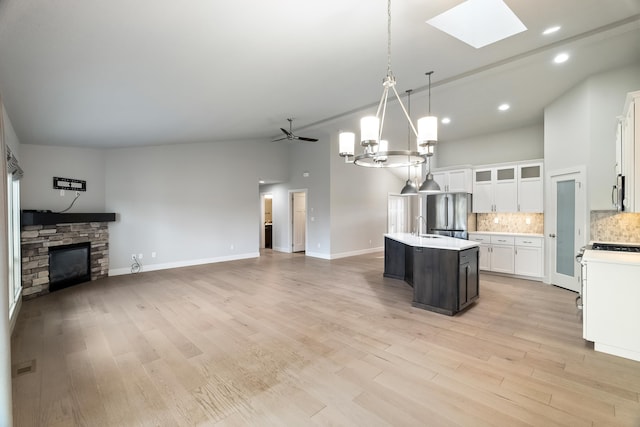 kitchen with a kitchen island with sink, ceiling fan, pendant lighting, a fireplace, and light hardwood / wood-style floors