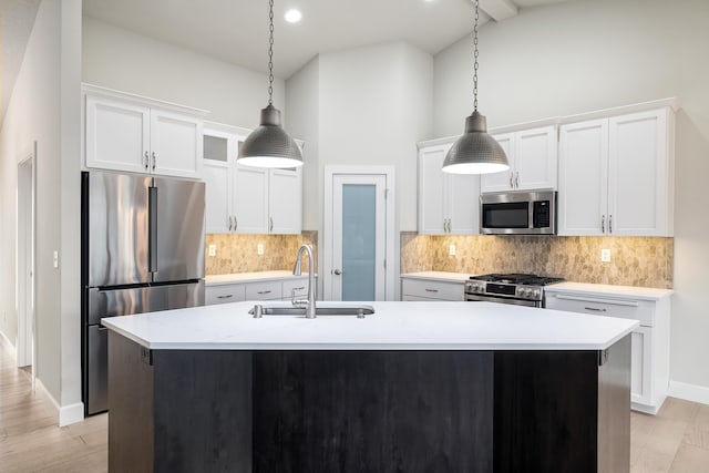 kitchen with white cabinetry, sink, stainless steel appliances, decorative light fixtures, and a kitchen island with sink