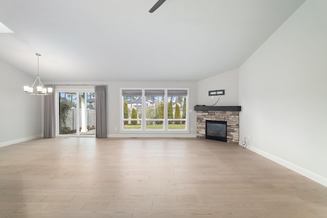 unfurnished living room featuring ceiling fan with notable chandelier, a stone fireplace, light wood-type flooring, and vaulted ceiling