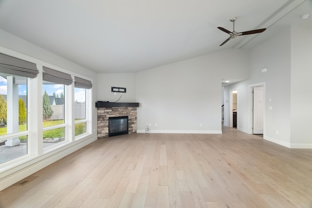 unfurnished living room featuring vaulted ceiling, light hardwood / wood-style flooring, ceiling fan, and a stone fireplace