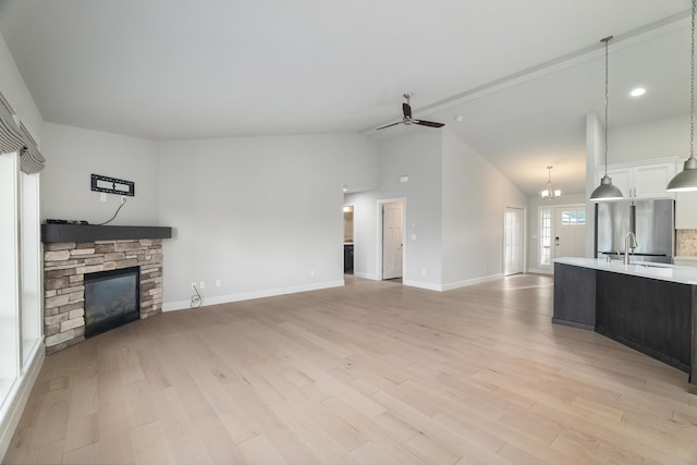 unfurnished living room with ceiling fan, sink, vaulted ceiling, a fireplace, and light wood-type flooring