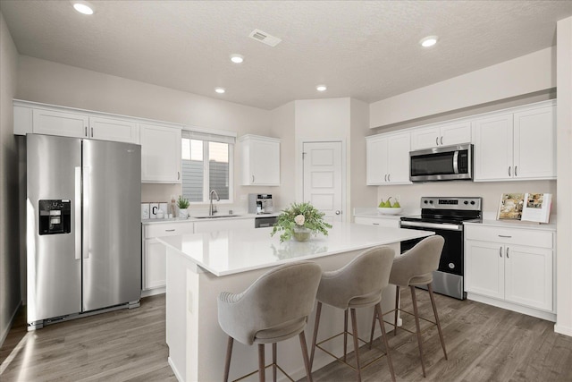 kitchen featuring white cabinetry, sink, appliances with stainless steel finishes, a kitchen island, and hardwood / wood-style flooring