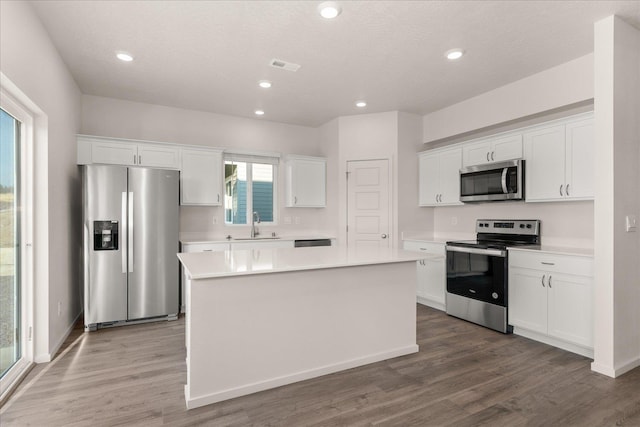 kitchen with stainless steel appliances, a kitchen island, sink, hardwood / wood-style floors, and white cabinetry