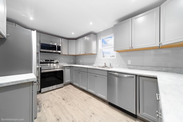 kitchen featuring sink, stainless steel appliances, light hardwood / wood-style floors, gray cabinets, and decorative backsplash