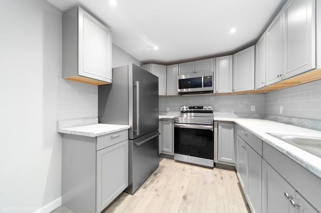 kitchen with sink, light hardwood / wood-style flooring, gray cabinets, tasteful backsplash, and stainless steel appliances