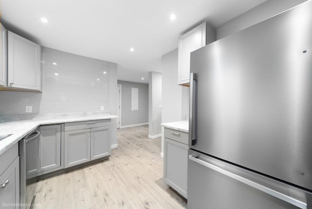 kitchen featuring backsplash, gray cabinetry, light wood-type flooring, and stainless steel appliances