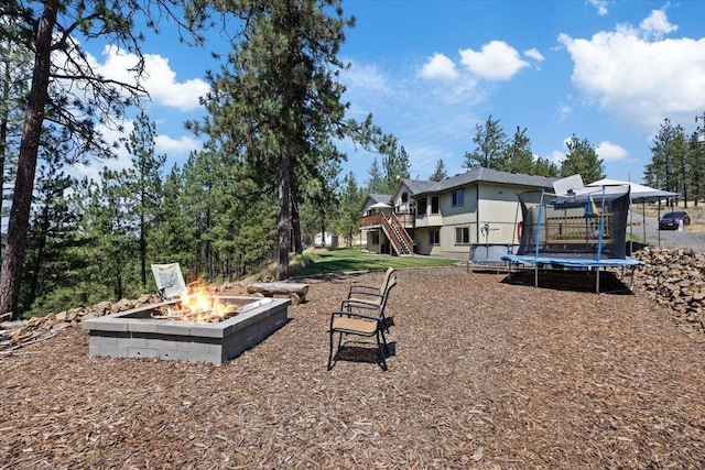 view of yard featuring a trampoline, a fire pit, and a wooden deck