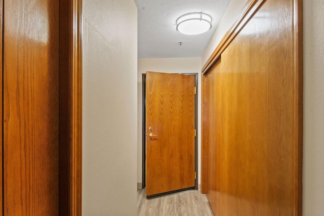 hallway with light hardwood / wood-style flooring and a textured ceiling