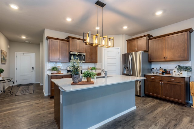 kitchen with sink, dark hardwood / wood-style floors, an island with sink, pendant lighting, and appliances with stainless steel finishes