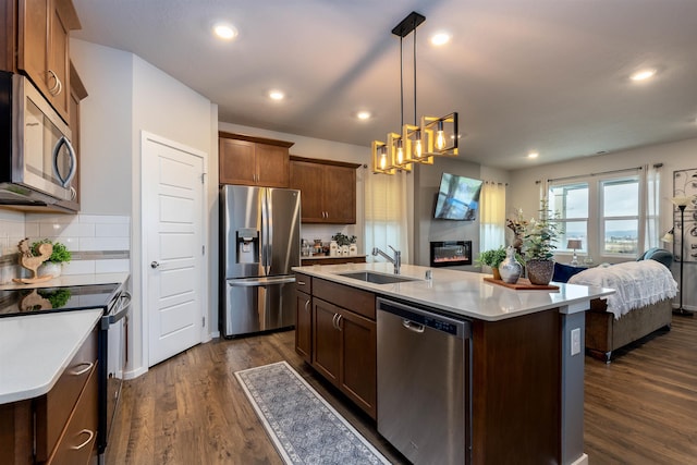 kitchen with tasteful backsplash, stainless steel appliances, sink, decorative light fixtures, and a center island with sink