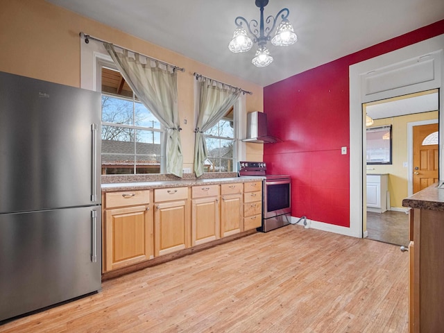 kitchen featuring hanging light fixtures, stainless steel appliances, wall chimney range hood, an inviting chandelier, and light hardwood / wood-style floors