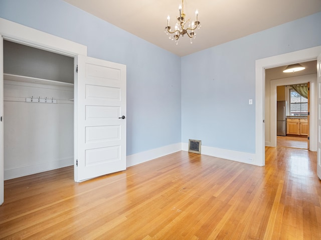 unfurnished bedroom with stainless steel fridge, light wood-type flooring, a closet, and a notable chandelier