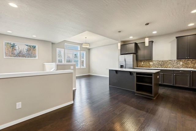 kitchen featuring backsplash, sink, stainless steel refrigerator with ice dispenser, hanging light fixtures, and a kitchen island