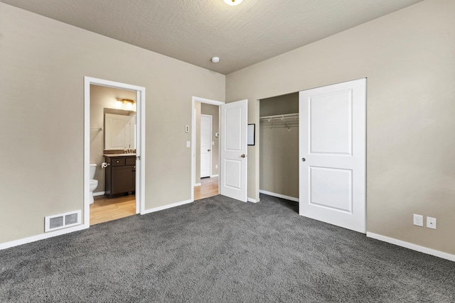 unfurnished bedroom featuring dark colored carpet, sink, ensuite bath, a textured ceiling, and a closet