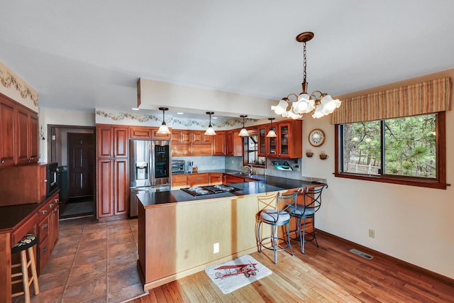 kitchen with kitchen peninsula, gas cooktop, sink, decorative light fixtures, and stainless steel fridge with ice dispenser