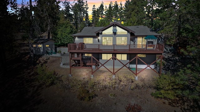 back house at dusk featuring a wooden deck and a storage shed