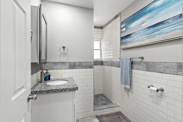 bathroom featuring a tile shower, vanity, and tile walls