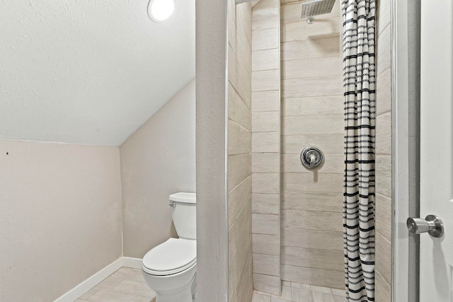 bathroom with tile patterned flooring, toilet, lofted ceiling, and a tile shower