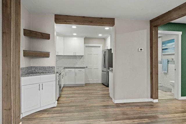 kitchen with decorative backsplash, light stone countertops, light wood-type flooring, white cabinetry, and stainless steel refrigerator